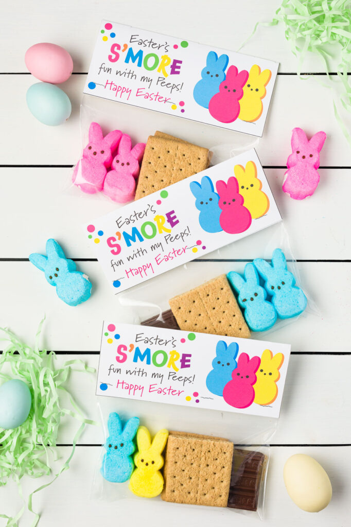 three Easter smore kits with peeps, graham cracker, and chocolate candy bar in a plastic bag with a paper graphic topper