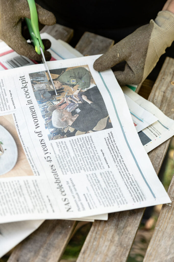 Using scissors to cut newspaper on a wooden table outside