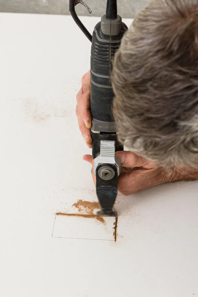 Using a oscillating saw to cut a hole in the smooth brown board for the electrical outlet