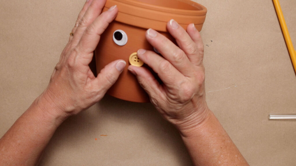 Glue on a button nose to the clay pot (head)