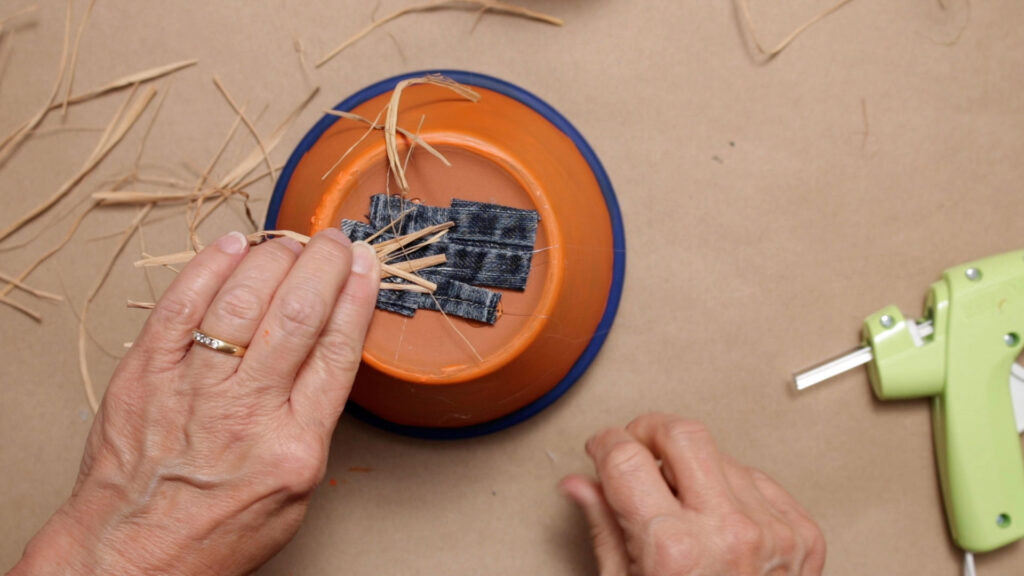 Glue fabric scraps and raffia on the top of the scarecrow body pot 