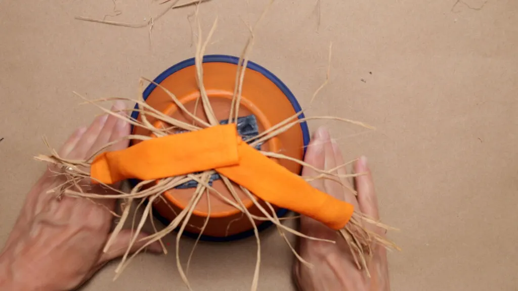 Attach arms to over the fabric scraps and raffia on the bottom of the clay pot