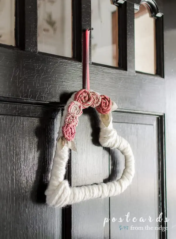 White yarn with pink fabric flowers hung on a black door