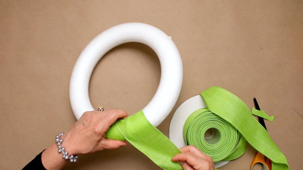 Wrapping green linen ribbon around a styrofoam wreath form 