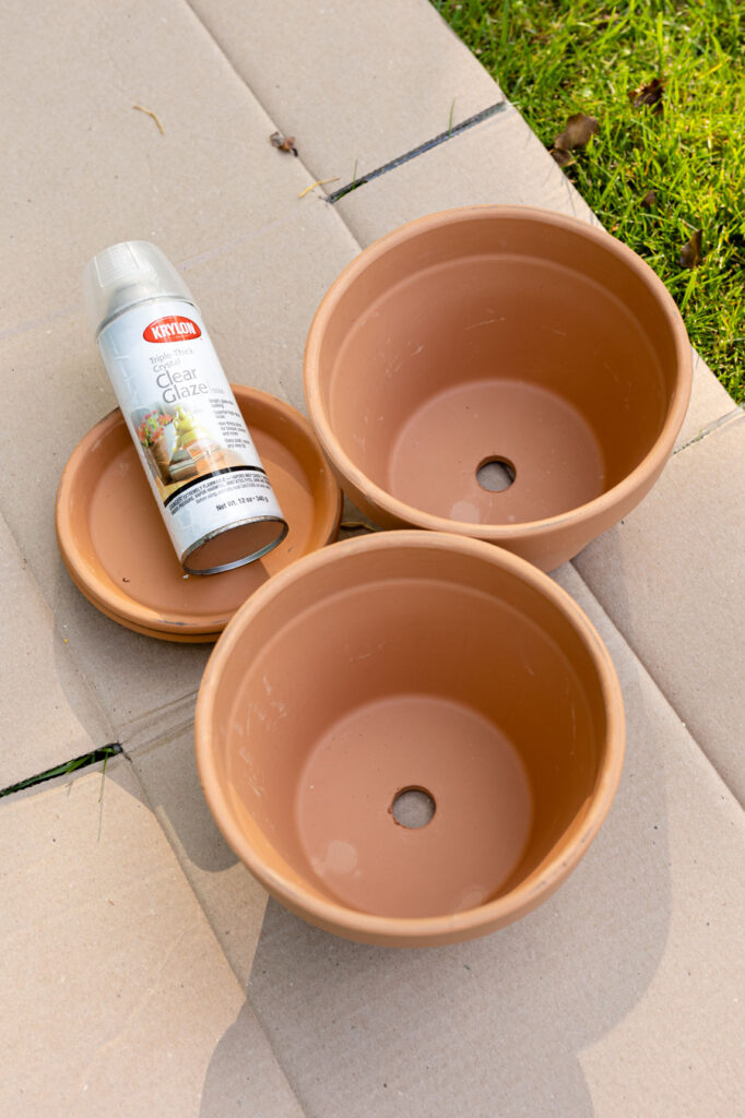 two clay pots, one clay saucer and a can of glaze on cardboard 