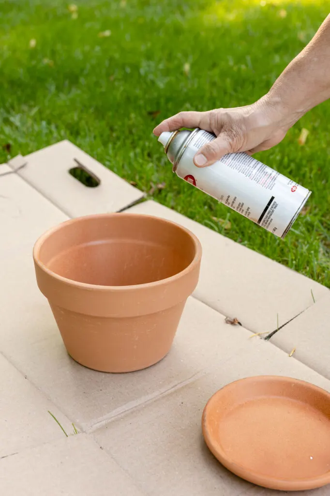 spraying a clay pot and saucer sitting on cardboard in the yard