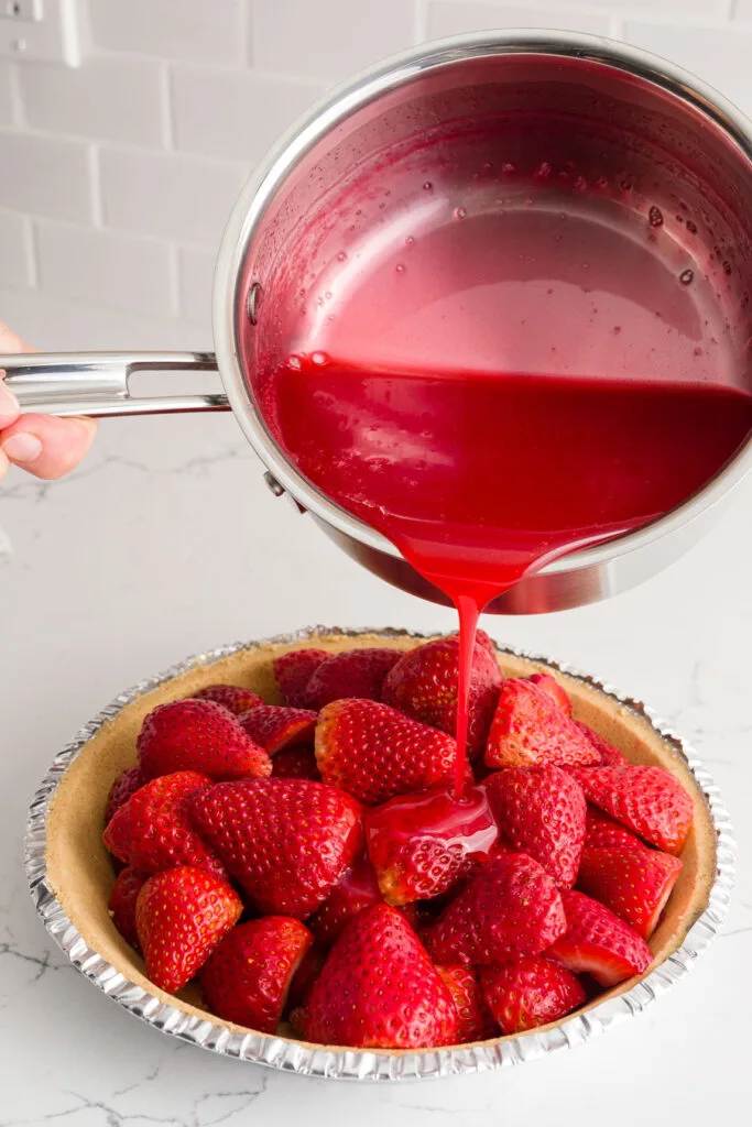 Pouring the jello mixture directly on the strawberries in the pie crust