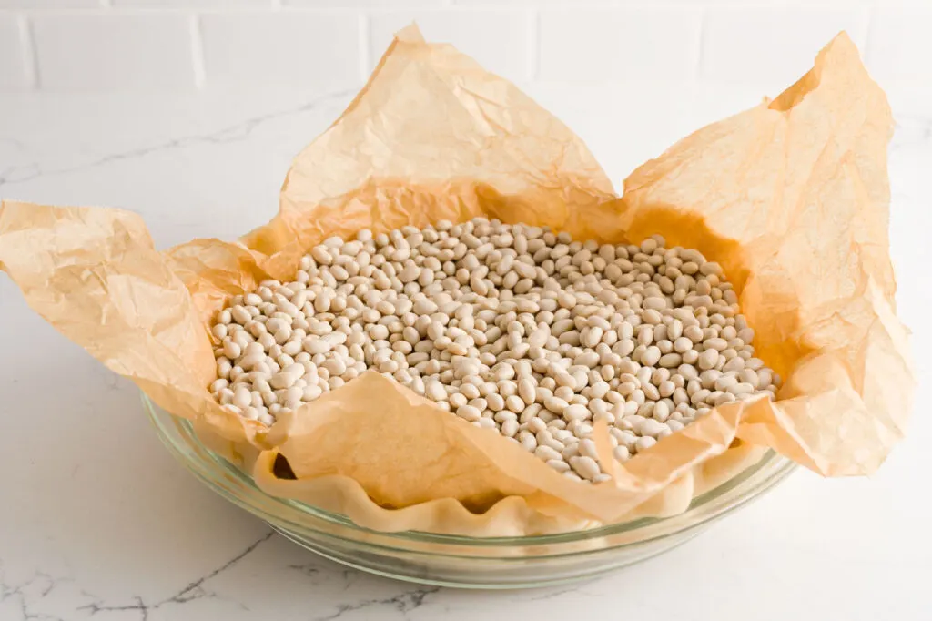 glass pie plate with a pie crust lined with a piece of parchment paper and dried beans