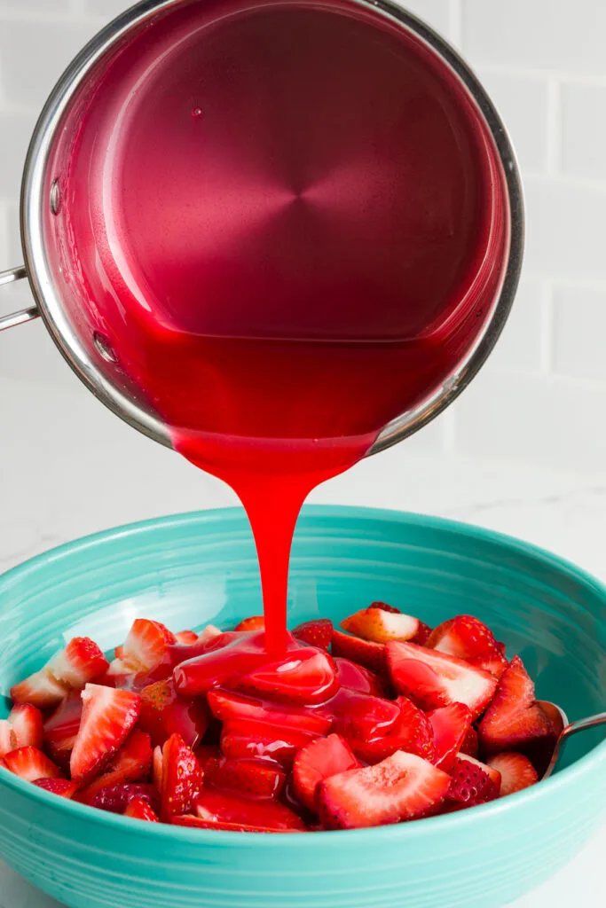 pouring the jello mixture on the strawberries in a large bowl