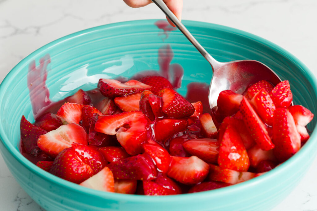 Mixing the strawberries with a spoon in a large bowl after pouring the jello mixture on them