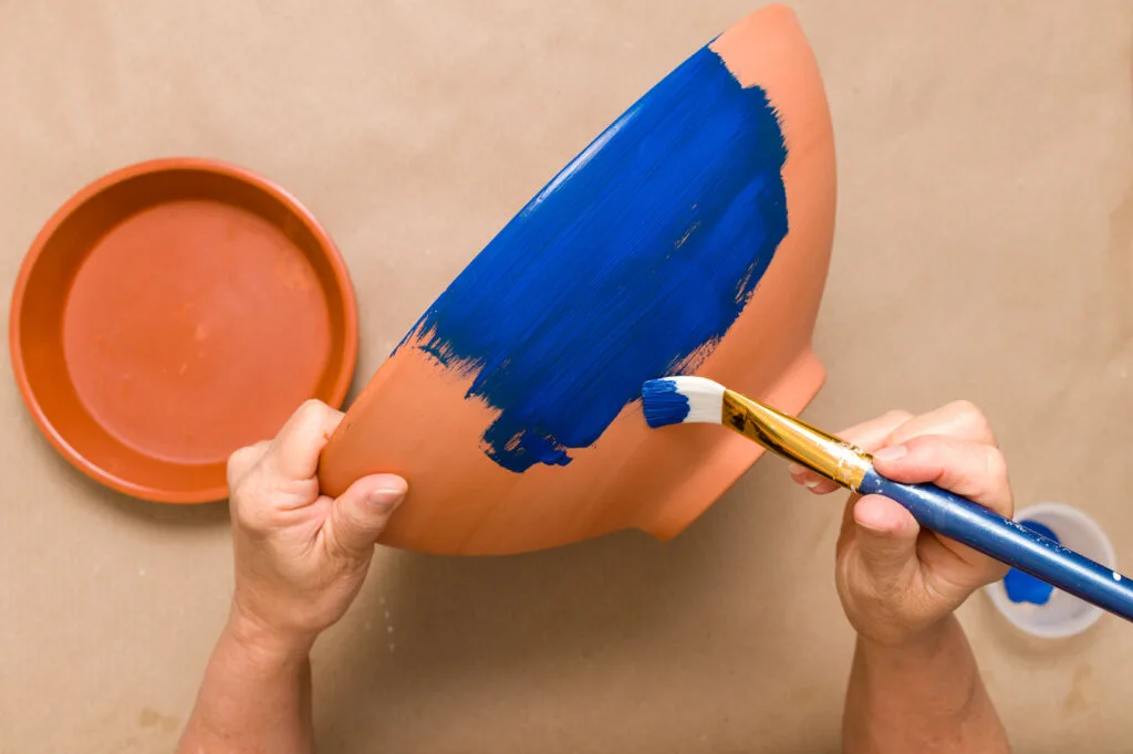 painting a clay pot with blue paint