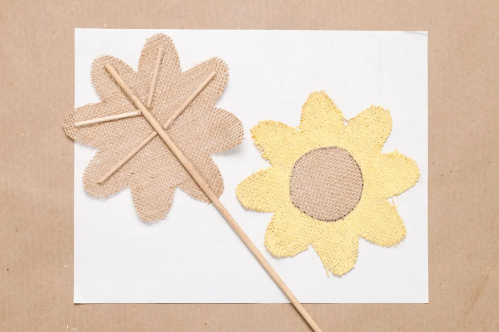 Back piece of fabric flower with the dowel supports and skewer stem and the painted flower front on a craft table