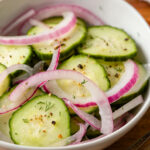 Red onion and cucumber salad in a bowl on a wood table
