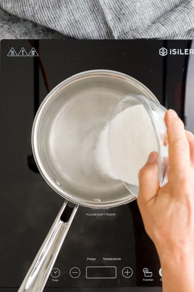 pouring sugar in a sauce pan over water