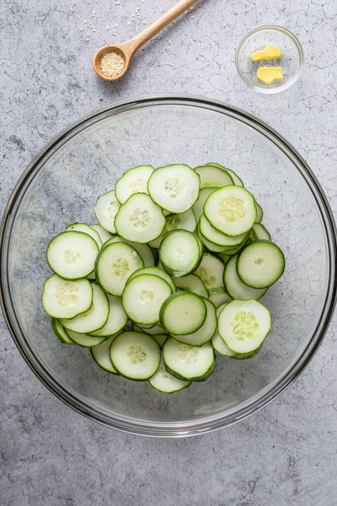cucumber slices in a bowl and a bowl with ginger slices and a spoon with sesame seeds