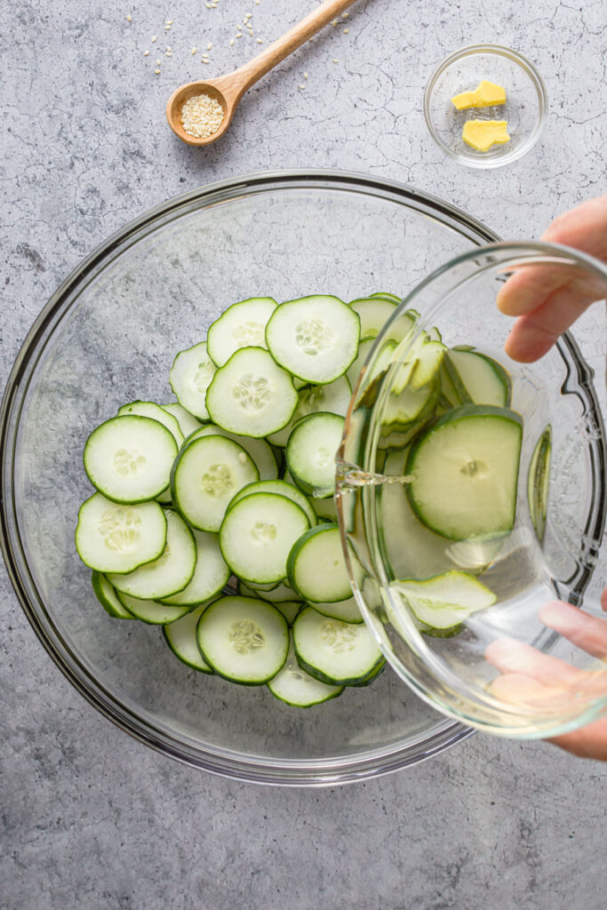Pouring the dressing over cucumber slices in a bowl