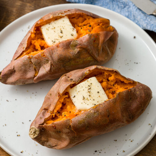 two baked sweet potatoes with butter on a plate