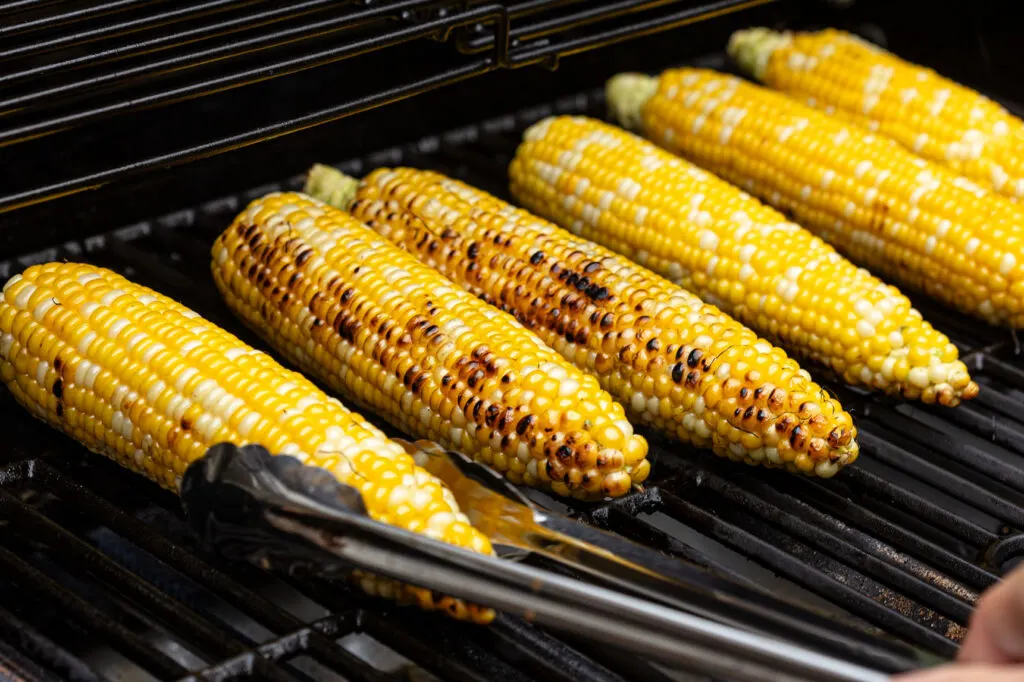 Turning grilled corn on the cob on the grill grates