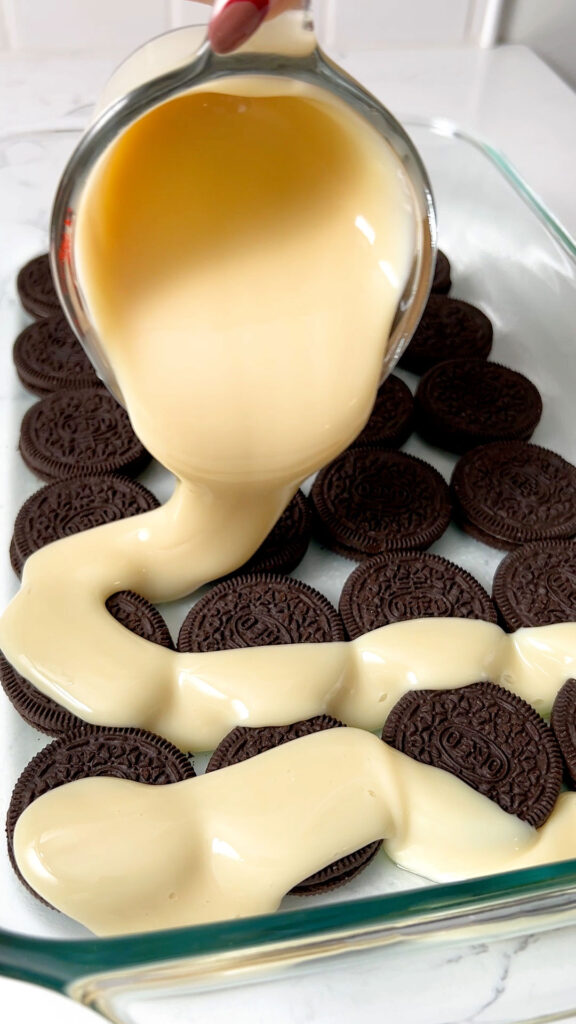 Pouring sweetened condensed milk over cookies in a baking dish
