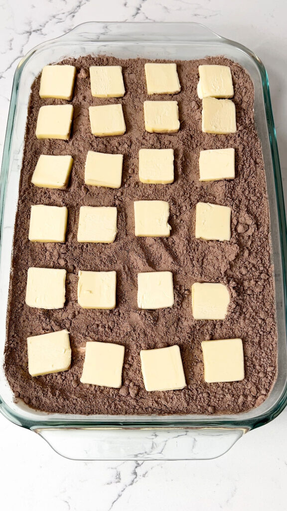 Pats of butter evenly distributed over the top of the cake mix