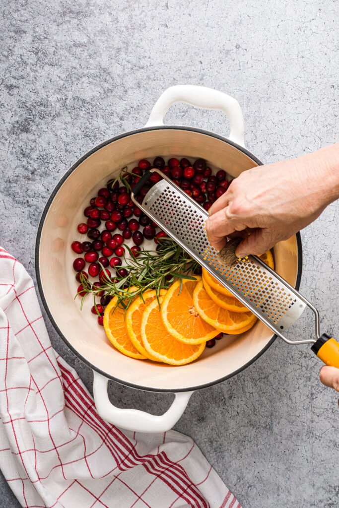 Grating whole nutmeg over the fresh ingredients in the pot