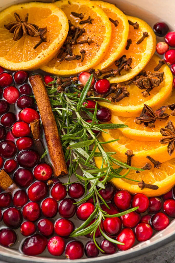 Pot filled with fresh cranberries, orange slices, rosemary, cinnamon sticks, nutmeg, cloves, star anise and water