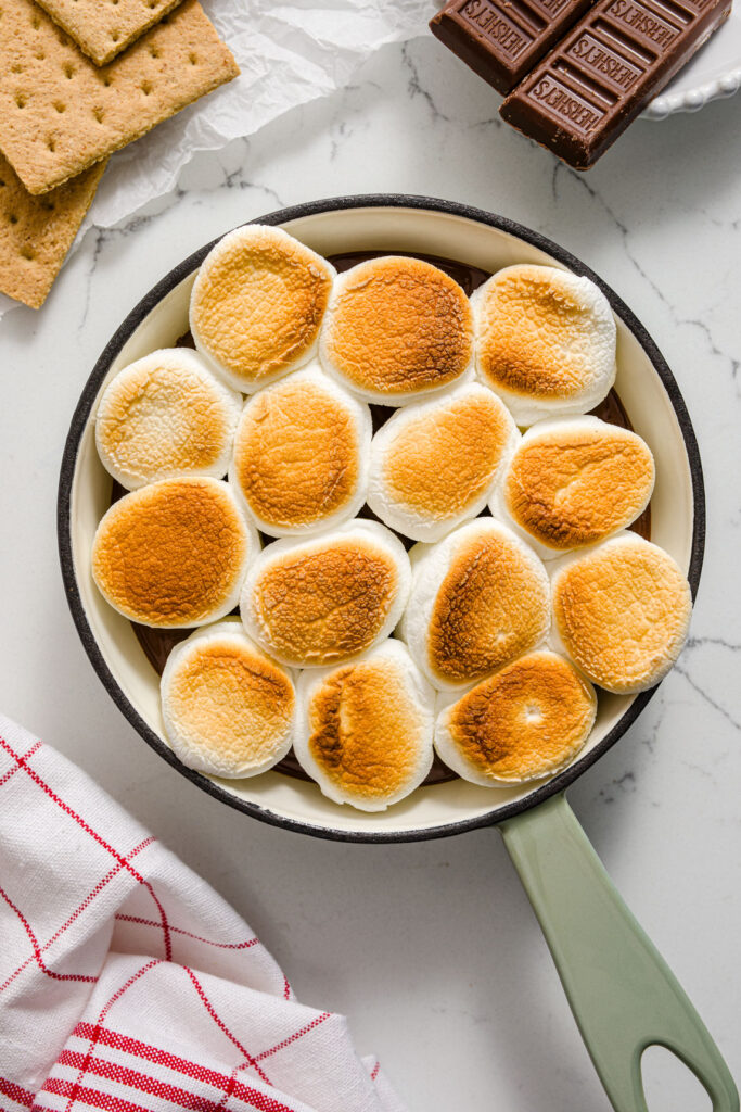 S'mores dip in a mini green and white iron skillet with graham crackers and chocolate bars