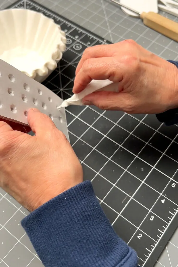 Inserting a folded and twisted coffee filter into a hole in the heart foam board