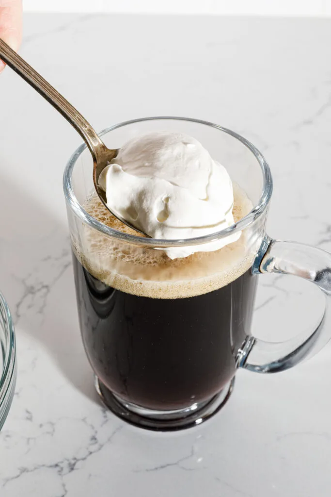 Spooning whipped cream onto the top of a cup of Irish coffee