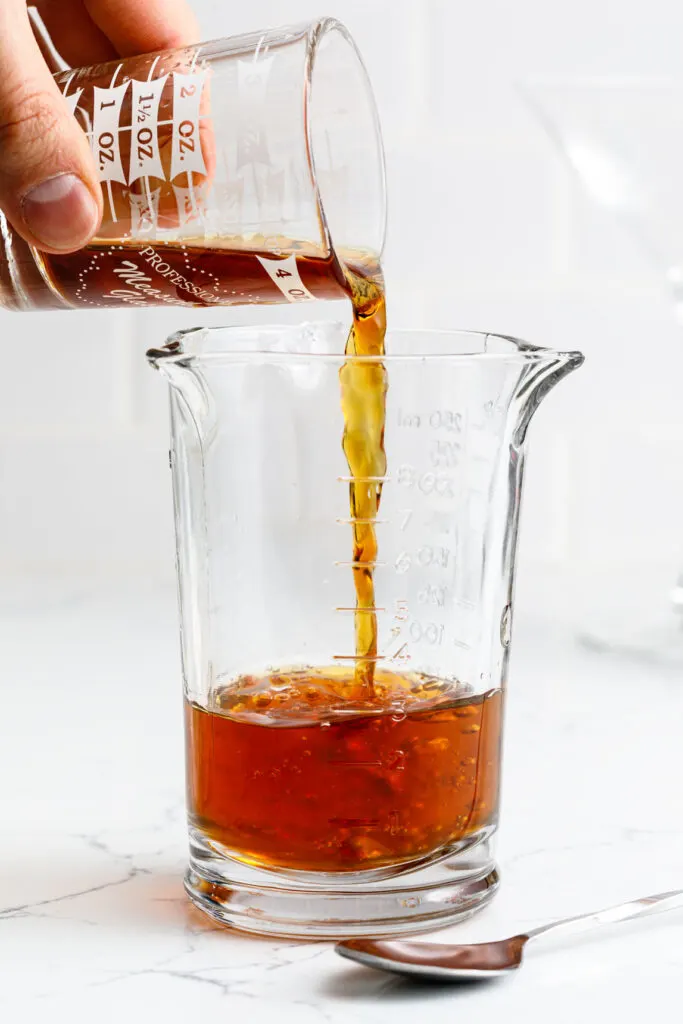 pouring sweet vermouth over rye whiskey in a graduated glass