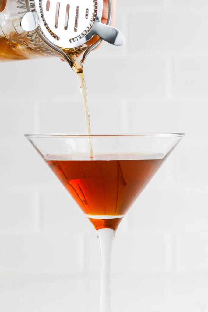 pouring a Manhattan cocktail into a glass through a cocktail strainer