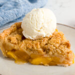 a slice of Peach crumble pie topped with a scoop of vanilla ice cream