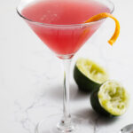 A cosmopolitan cocktail in a martini glass with a twist of orange