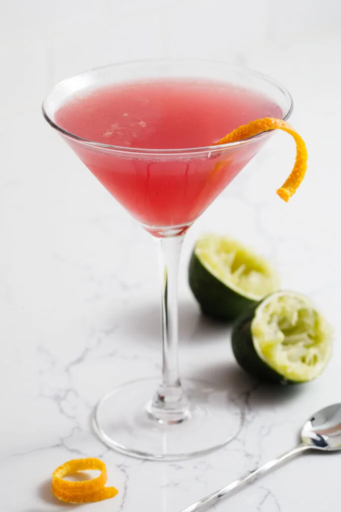 A cosmopolitan cocktail in a martini glass with a twist of orange