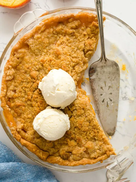 Peach Crumble pie with vanilla ice cream in a glass pie plate