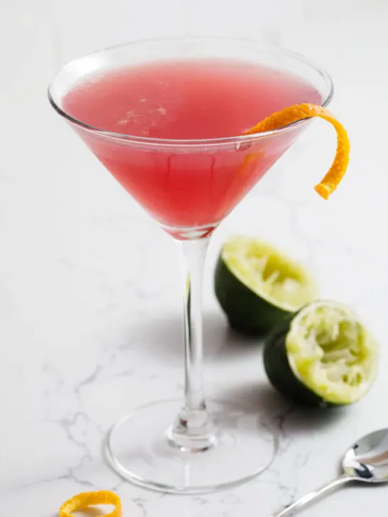 A cosmopolitan cocktail in a martini glass with a twist of orange
