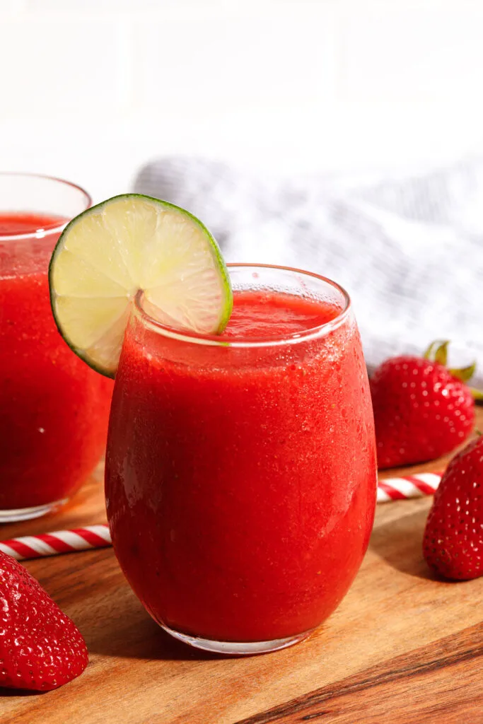 A strawberry daiquiri in a stemless wine glass with a wheel of lime on the rim