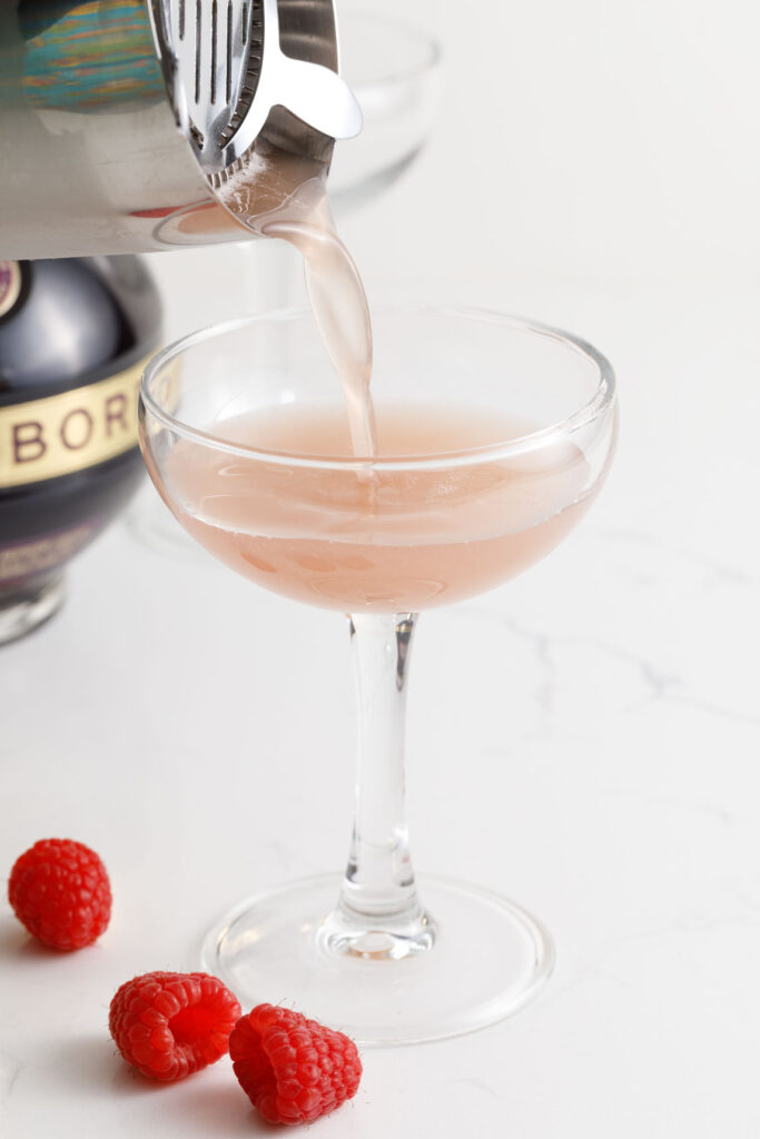 straining and pouring the shaken cocktail in a coupe glass