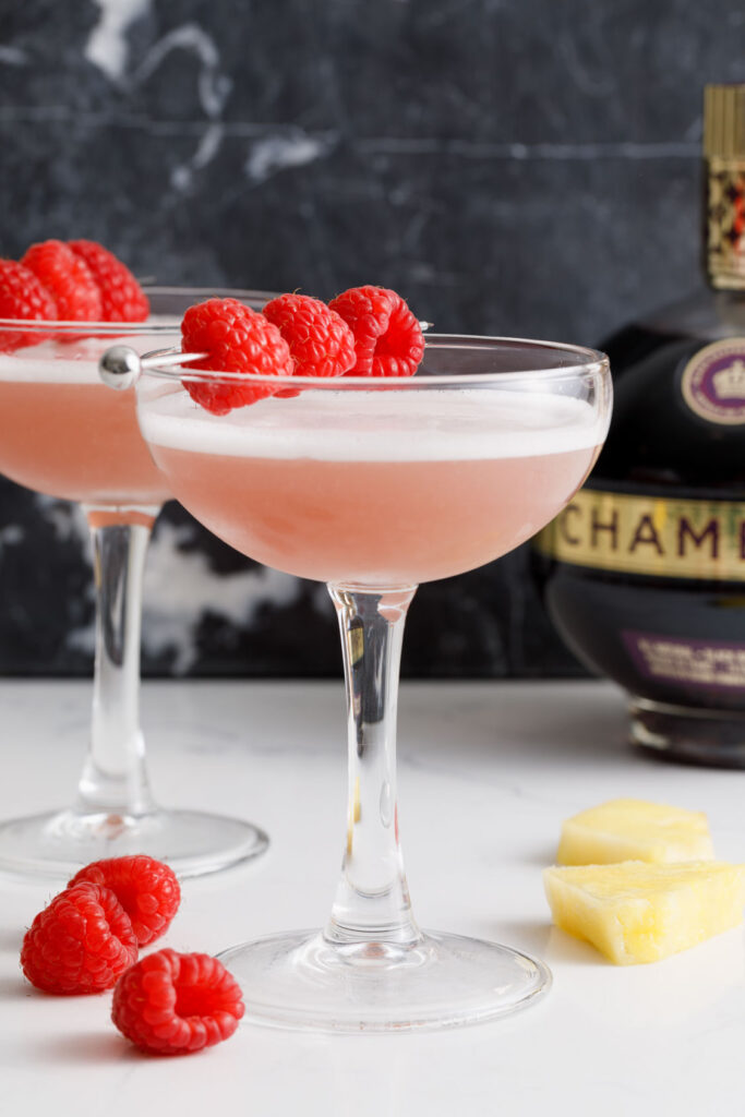 Two French Martinis on a counter with raspberries, pineapple