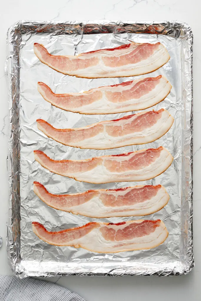 raw bacon on a foil lined baking sheet pan