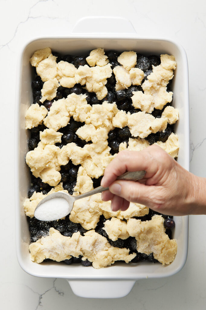 Sprinkling sugar over the blueberry cobbler
