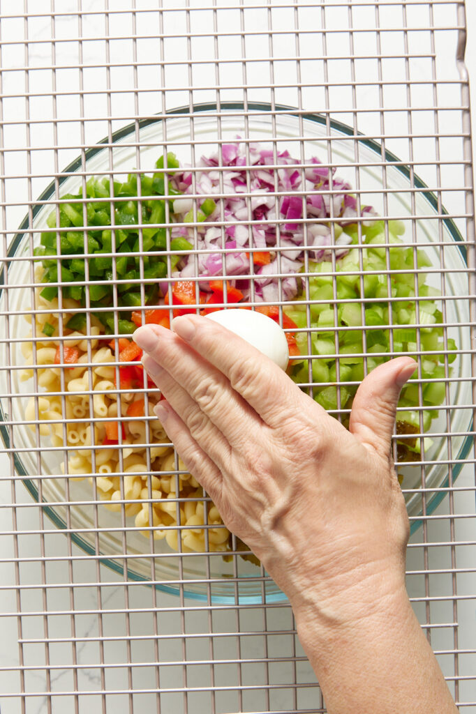 Pushing hard boiled eggs through a wire rack over a bowl