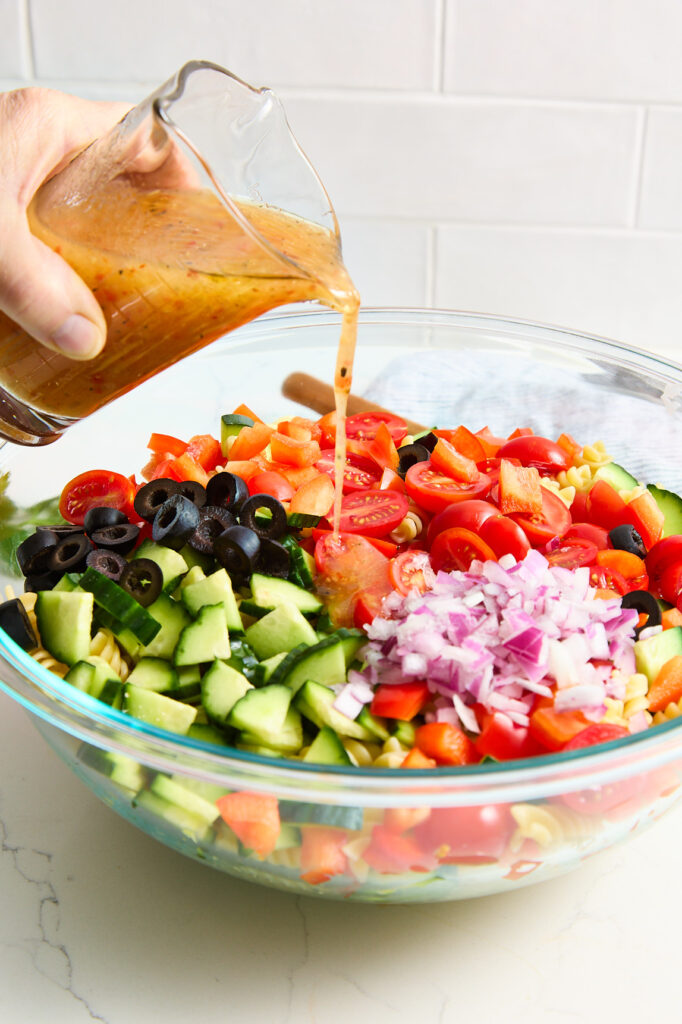 Pouring salad dressing over the pasta and vegetable mixture